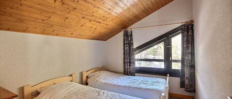 Un dormitorio con dos camas de madera, una ventana con cortinas y techo de madera.