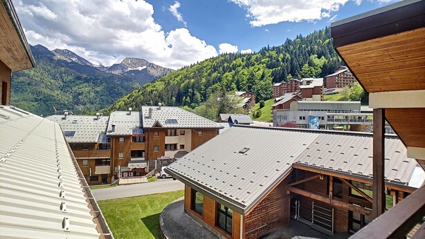A view of a hotel with multiple buildings, a green lawn, and mountains in the background.