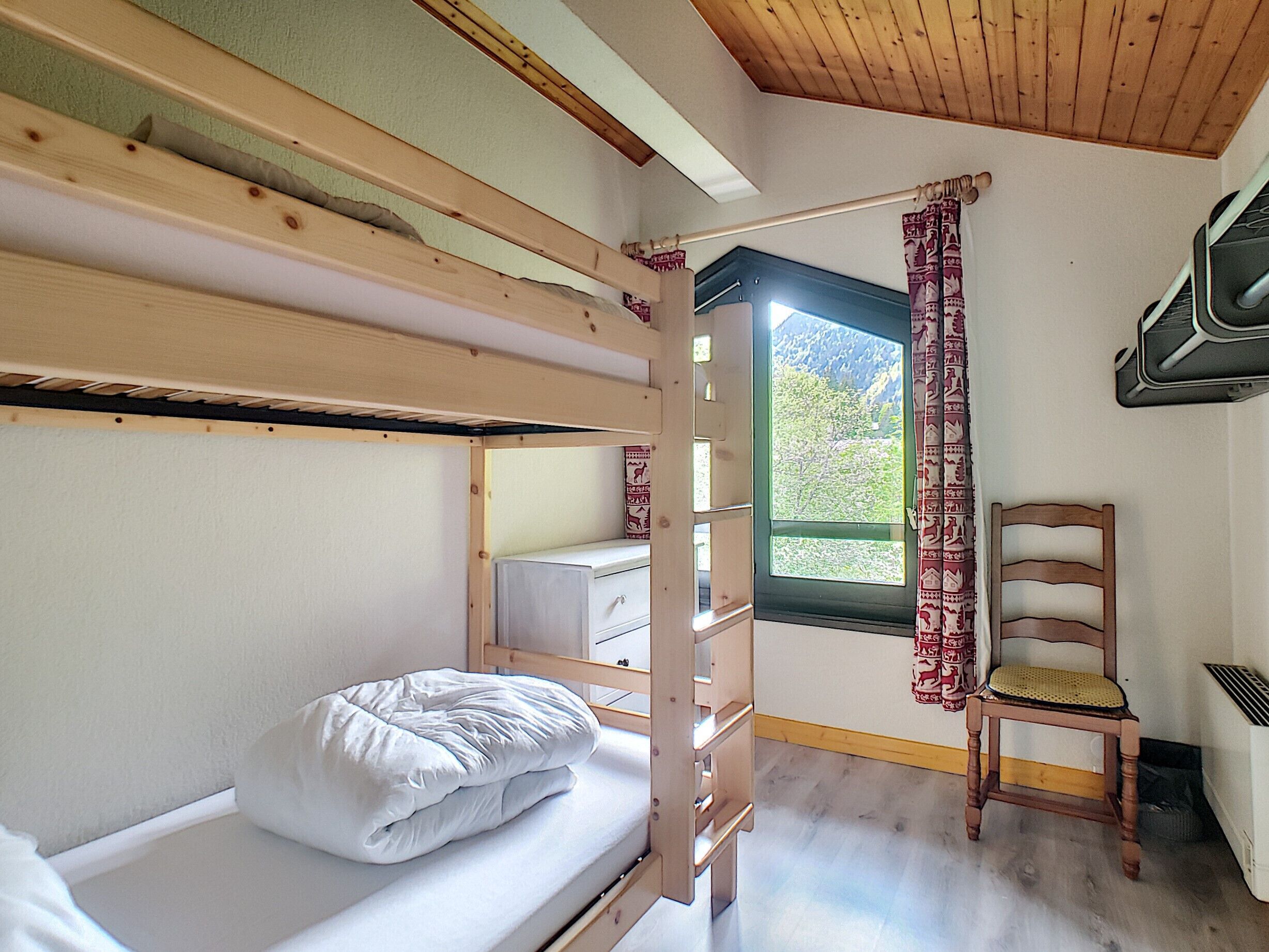 Une chambre avec un lit superposé, une fenêtre, une chaise et une petite table.