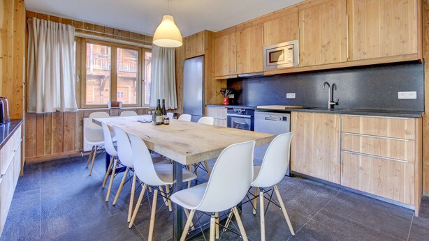 Une cuisine moderne avec des meubles de rangement en bois, une table à manger avec des chaises et une grande fenêtre avec des rideaux.