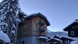 Un edificio in legno a più piani con balconi, circondato da alberi innevati e un paesaggio montuoso.