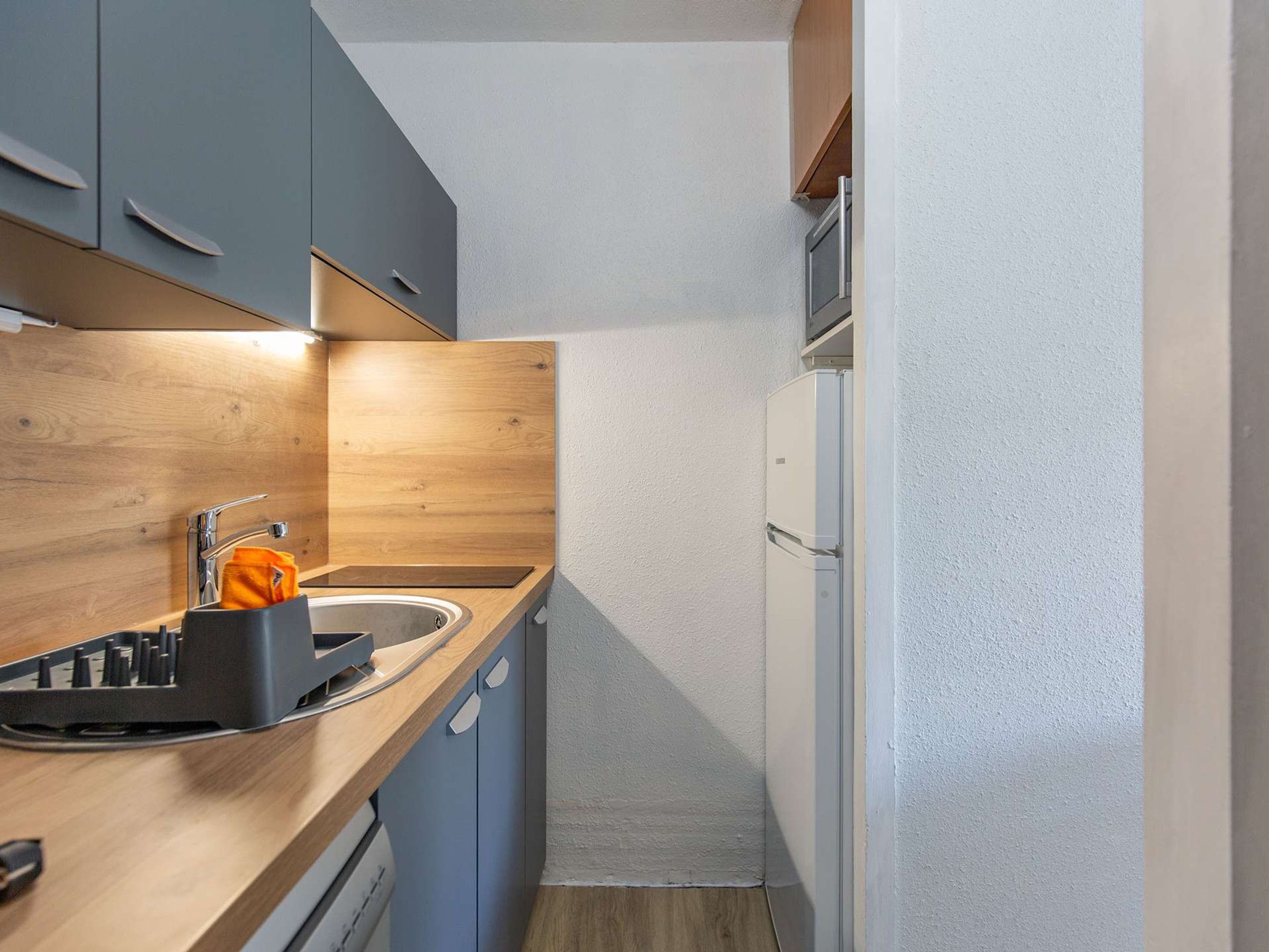 A compact kitchen with a sink, a dish rack, and a refrigerator.