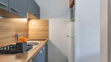 A compact kitchen with a sink, a dish rack, and a refrigerator.