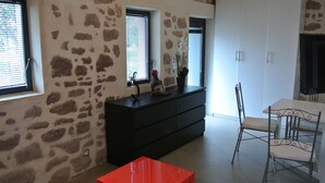 A room with stone walls, a black dresser, a red table, and a white chair. - Melko Kivimökki (Puget-sur-Argens)