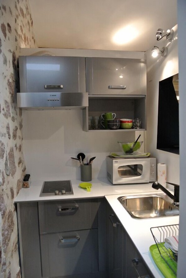 A compact kitchen with grey cabinets, a microwave, a sink, and a dish rack.