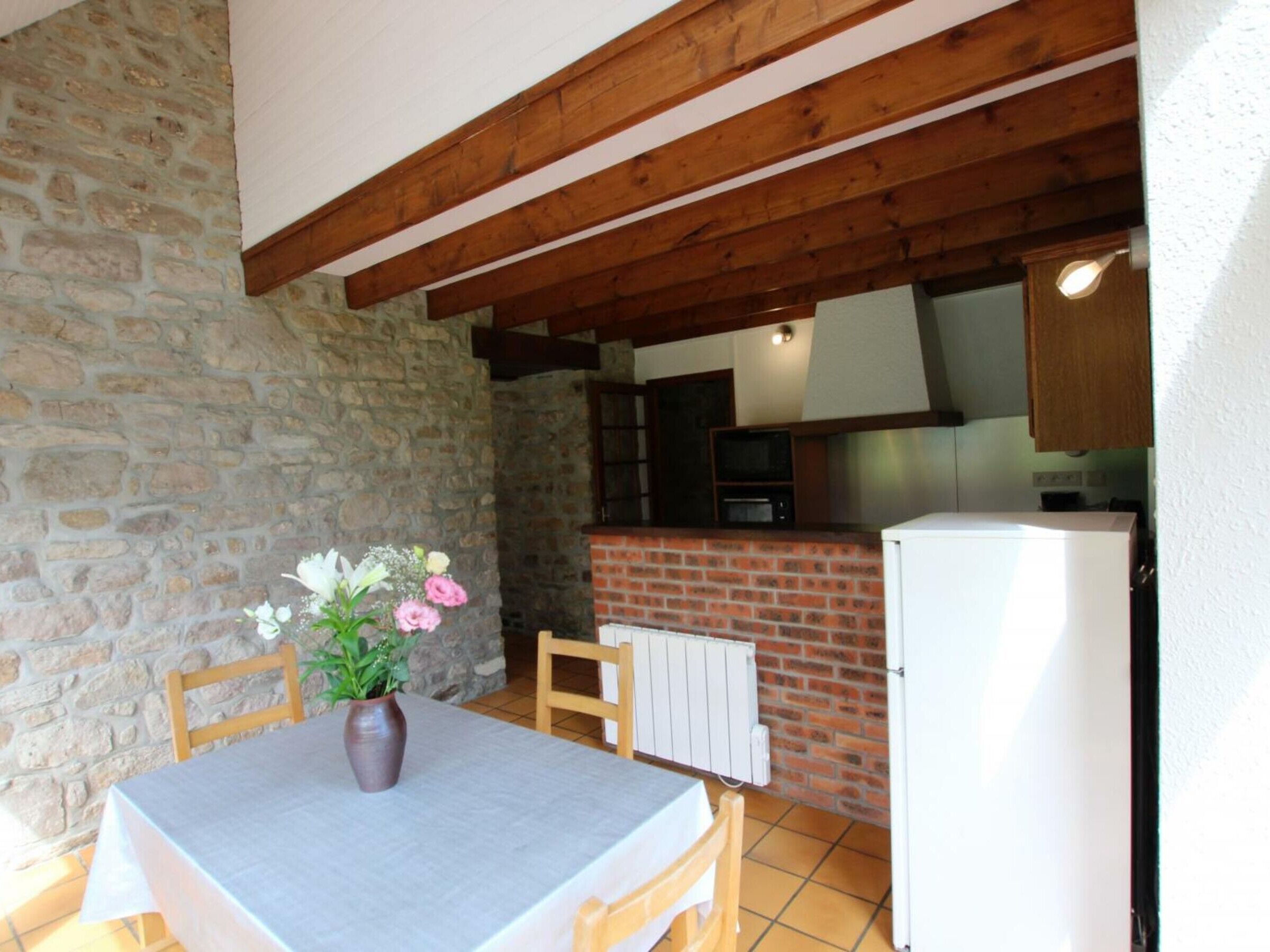 Una pared de piedra, vigas de madera, una chimenea de ladrillo, un refrigerador blanco y una mesa con sillas.