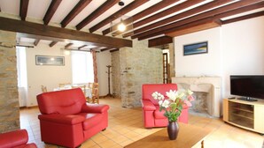 A living room with red sofas, a wooden coffee table, a stone wall, a fireplace, and a television.