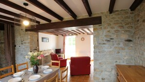 A dining area with a stone wall, wooden beams, a table set for four, and a red sofa.