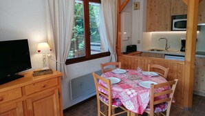 Una habitación acogedora con una mesa de comedor para dos, un televisor y una cocina con armarios de madera y un microondas.