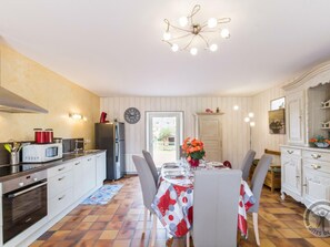 A modern kitchen with a dining area, featuring a clock, a refrigerator, a stove, and a chandelier.