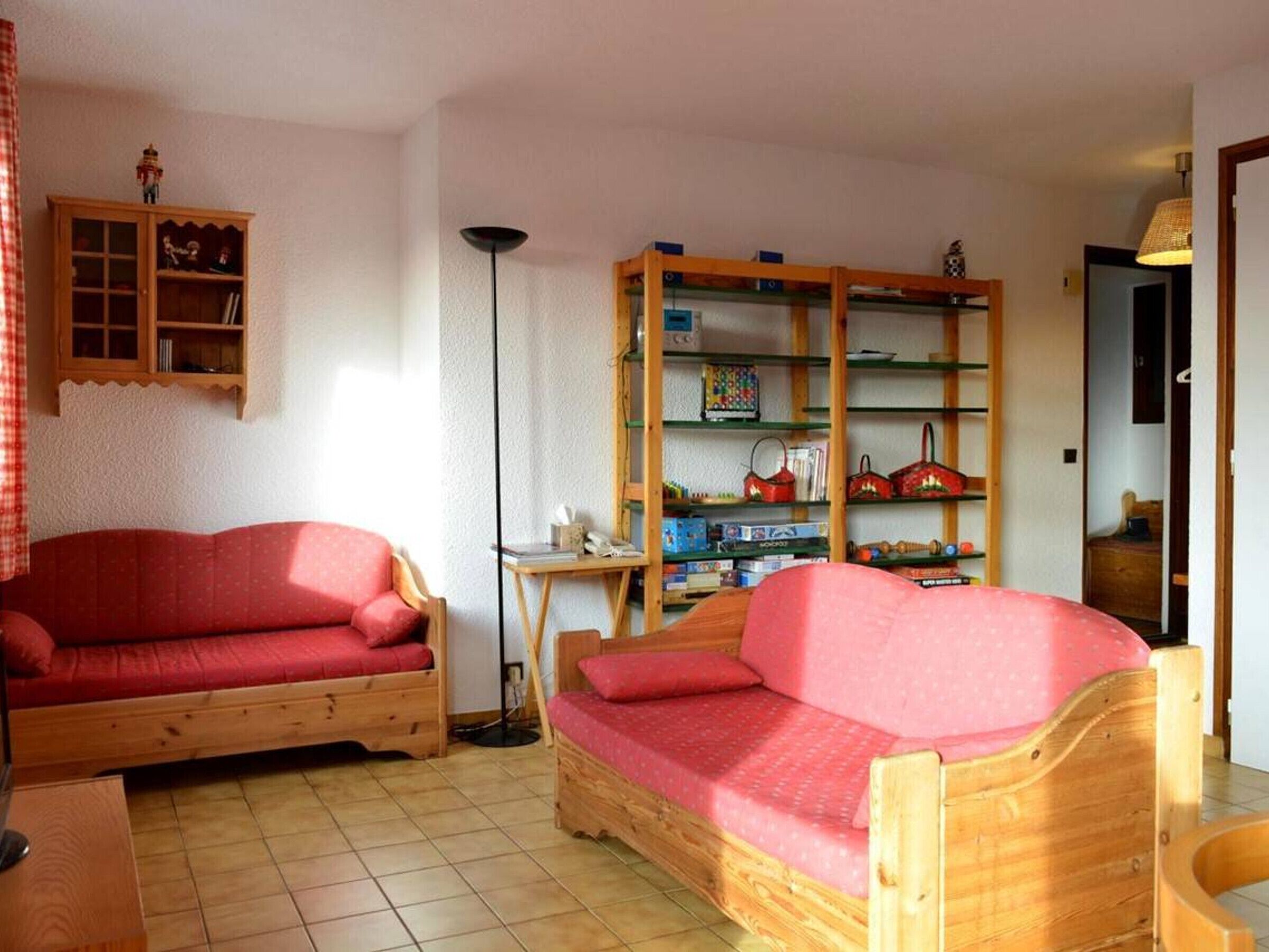 A cozy room with two wooden sofas, a small table, and a bookshelf filled with books and decorative items.