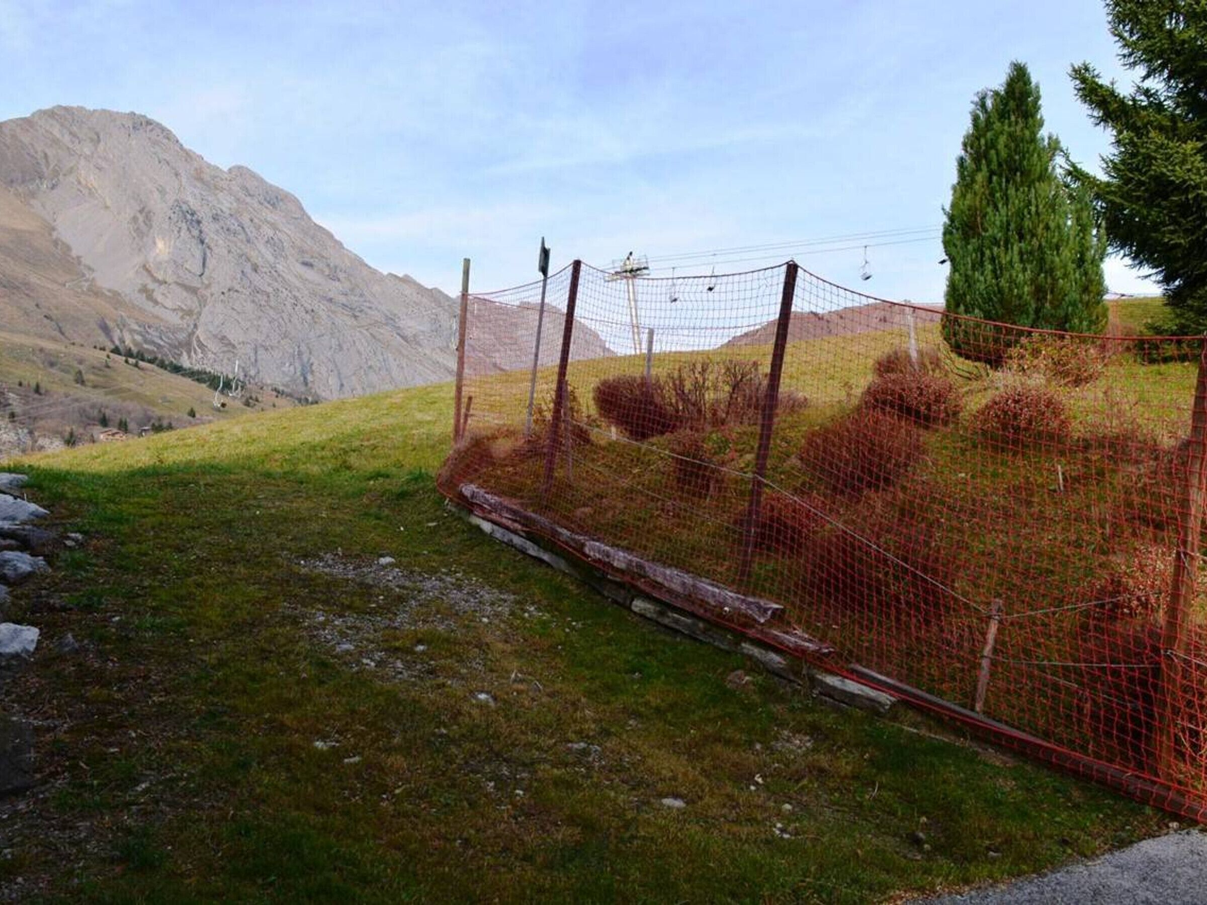Un espace délimité par une clôture, avec une chaîne de montagnes en arrière-plan, un champ d’herbe et un poteau de clôture en bois.