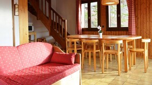 Una habitación acogedora con una escalera de madera, una mesa de comedor con sillas, un sofá rojo y una lámpara colgante.