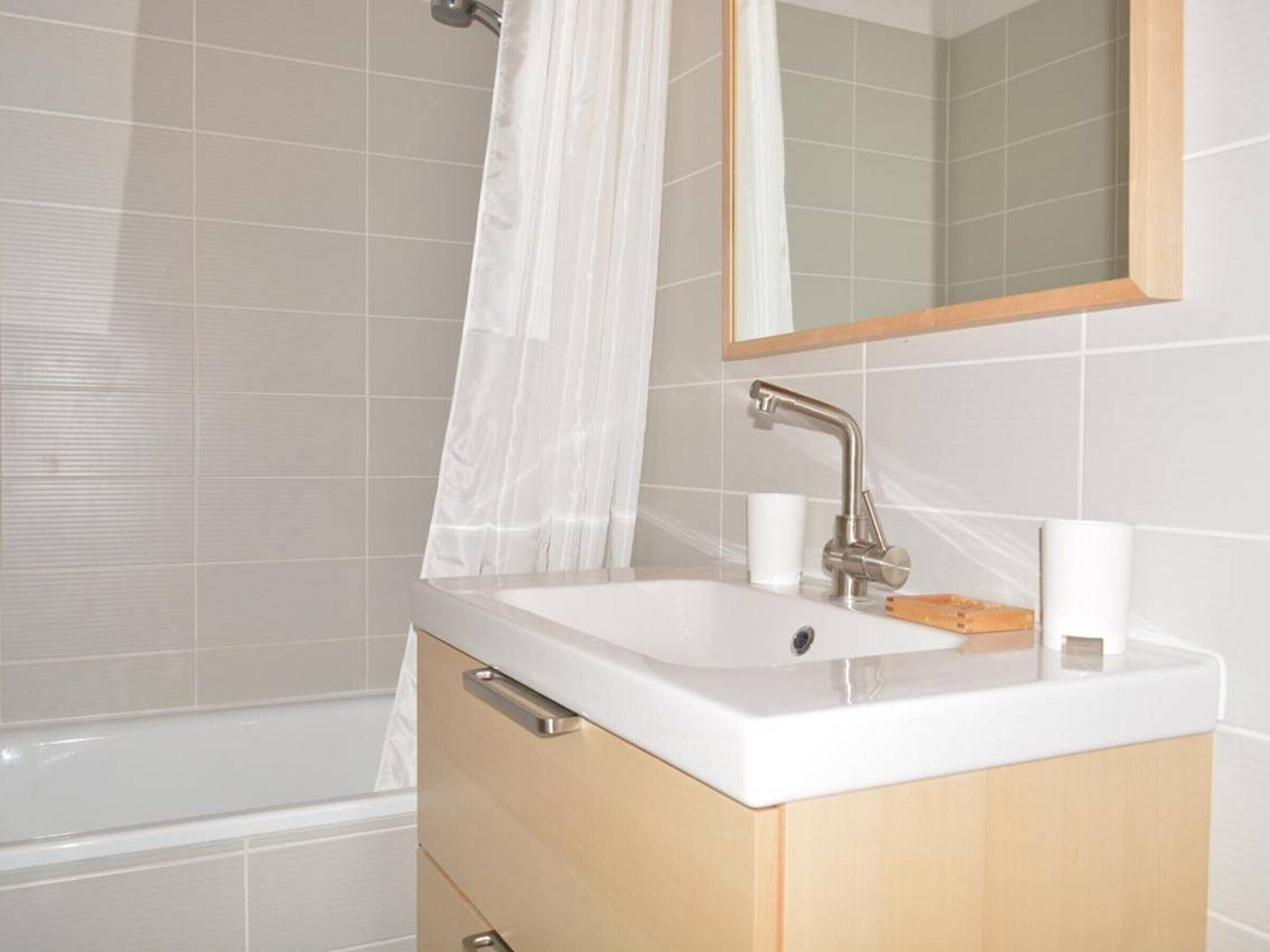 A bathroom with a white sink, wooden cabinet, and a mirror above it.