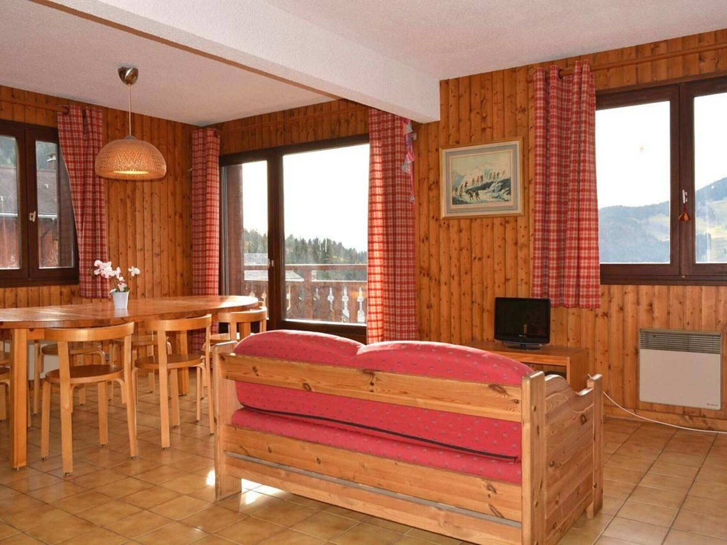 Ein Zimmer mit Holzboden, einem Bett, einem Esstisch mit Stühlen, einem Fernseher und einem Fenster mit Bergblick.