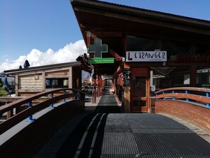 A train station platform with a wooden structure, a sign for 'L'etranger Lounge Bar', and a green sign indicating 'EN BOUT DE TERRASSE'.