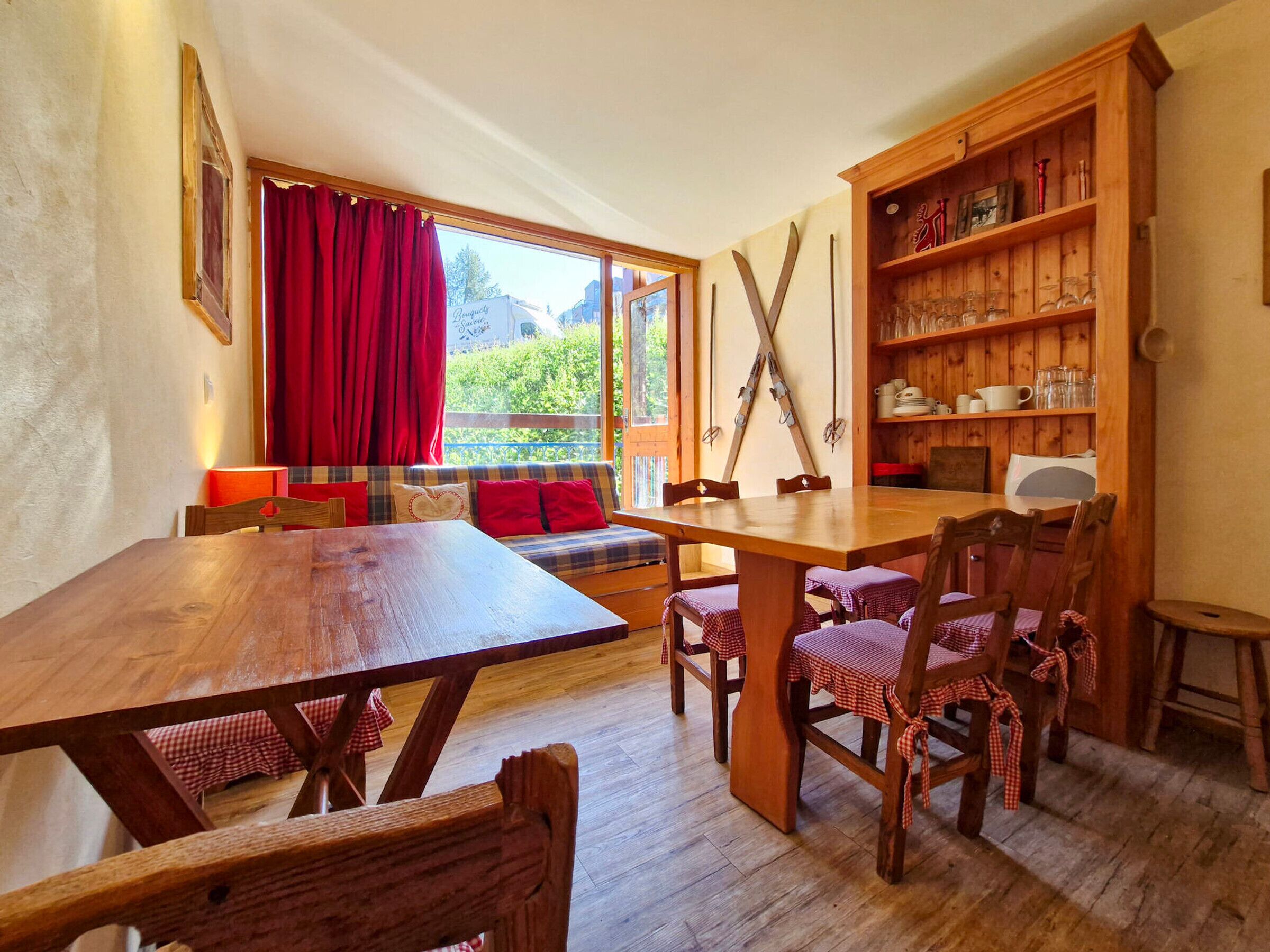 Un comedor acogedor con una mesa y sillas de madera, un sofá con cojines rojos y un estante de madera con utensilios de cocina.
