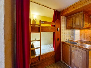 A bunk bed with a wooden ladder, a sink, and cabinets in a compact room.