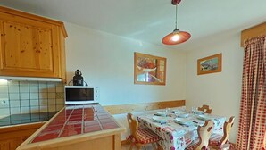 A kitchen with wooden cabinets, a microwave, and a tiled backsplash. There is a dining table with chairs and a hanging light fixture. - 3-room apt, sleeps 6, near shops and slopes, parking included, pets allowed (Le Grand-Bornand)