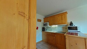 A kitchen with wooden cabinets, a microwave, and a kettle. - 3-room apt, sleeps 6, near shops and slopes, parking included, pets allowed (Le Grand-Bornand)