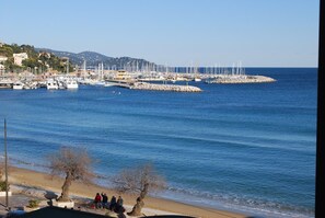 Un port de plaisance sur la côte, avec des bateaux amarrés, une plage de sable et quelques personnes assises au bord de l’eau.