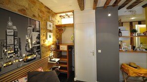 Et værelse med synlige træbjælker, et bybillede-plakat, et skrivebord med lampe og en garderobe.