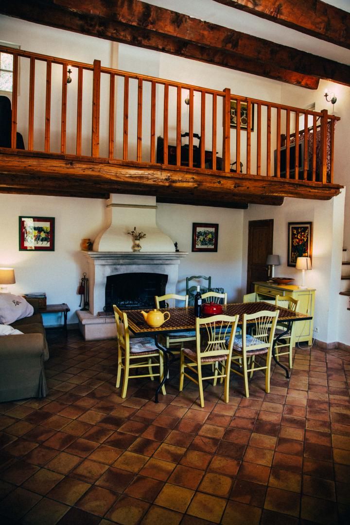 A cozy living room with a fireplace, wooden ceiling beams, and a dining area with chairs and a table.