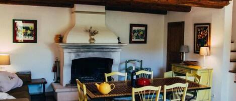 A cozy living room with a fireplace, wooden ceiling beams, and a dining area with chairs and a table.