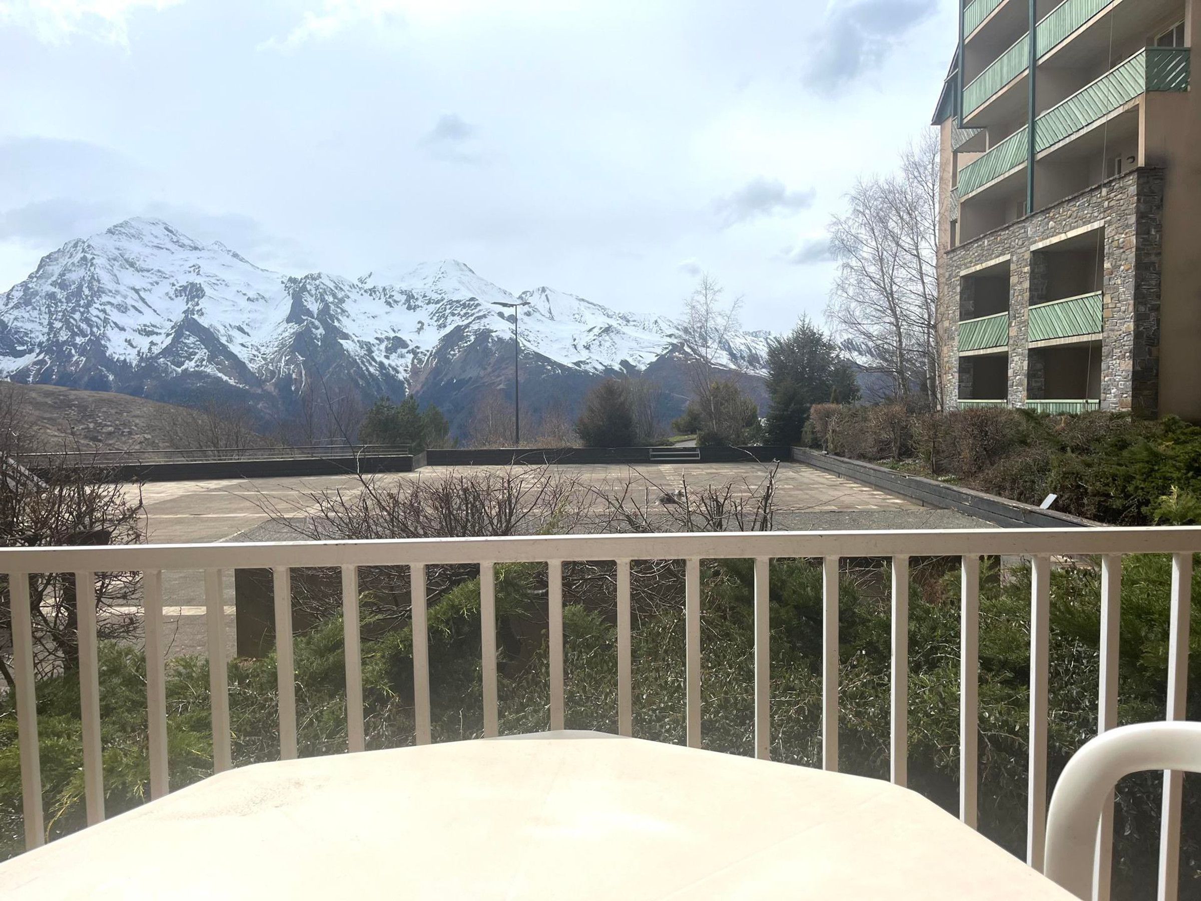 A balcony with a view of snow-capped mountains, a parking area, and a building with green awnings.