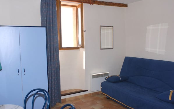 Una habitación con un sofá azul, un armario blanco, una ventana con cortinas y un radiador.