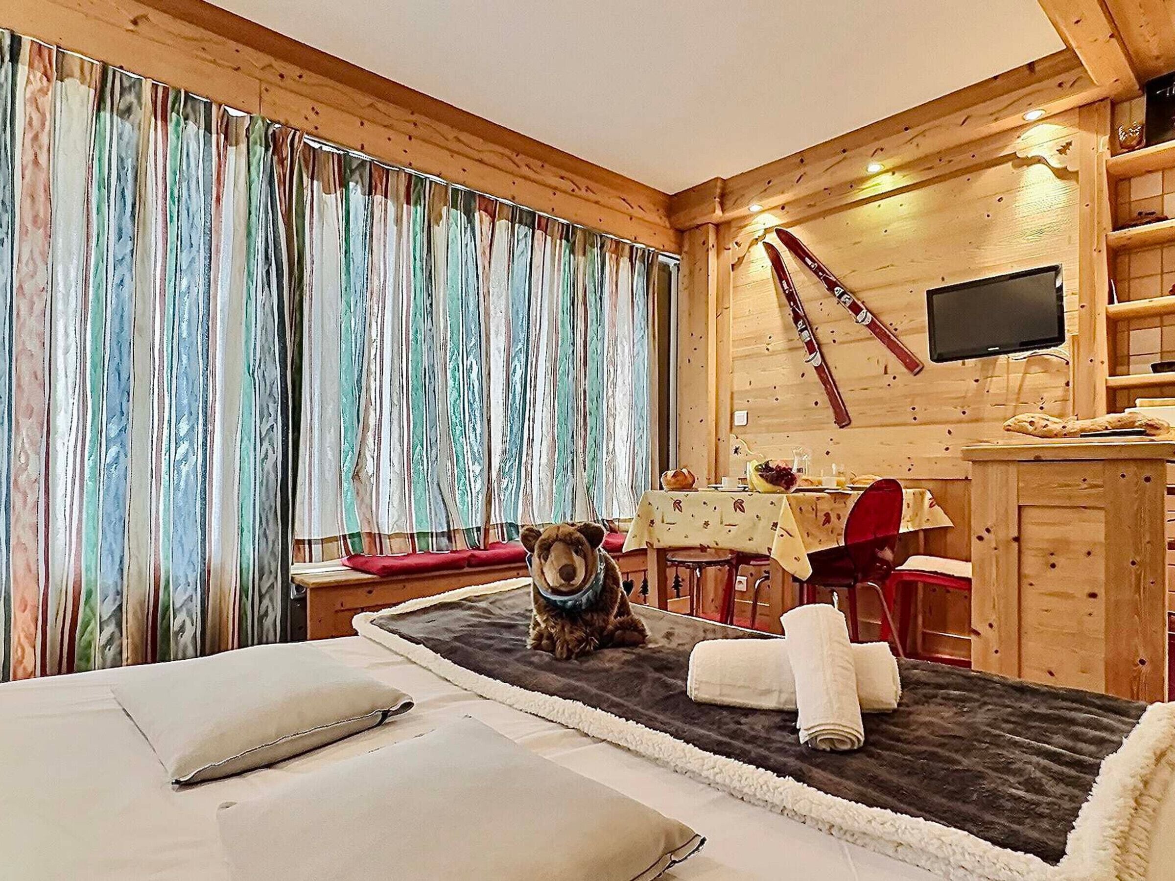 Een gezellige kamer met houten inrichting, een eettafel met stoelen, een televisie en een hond met een vest.