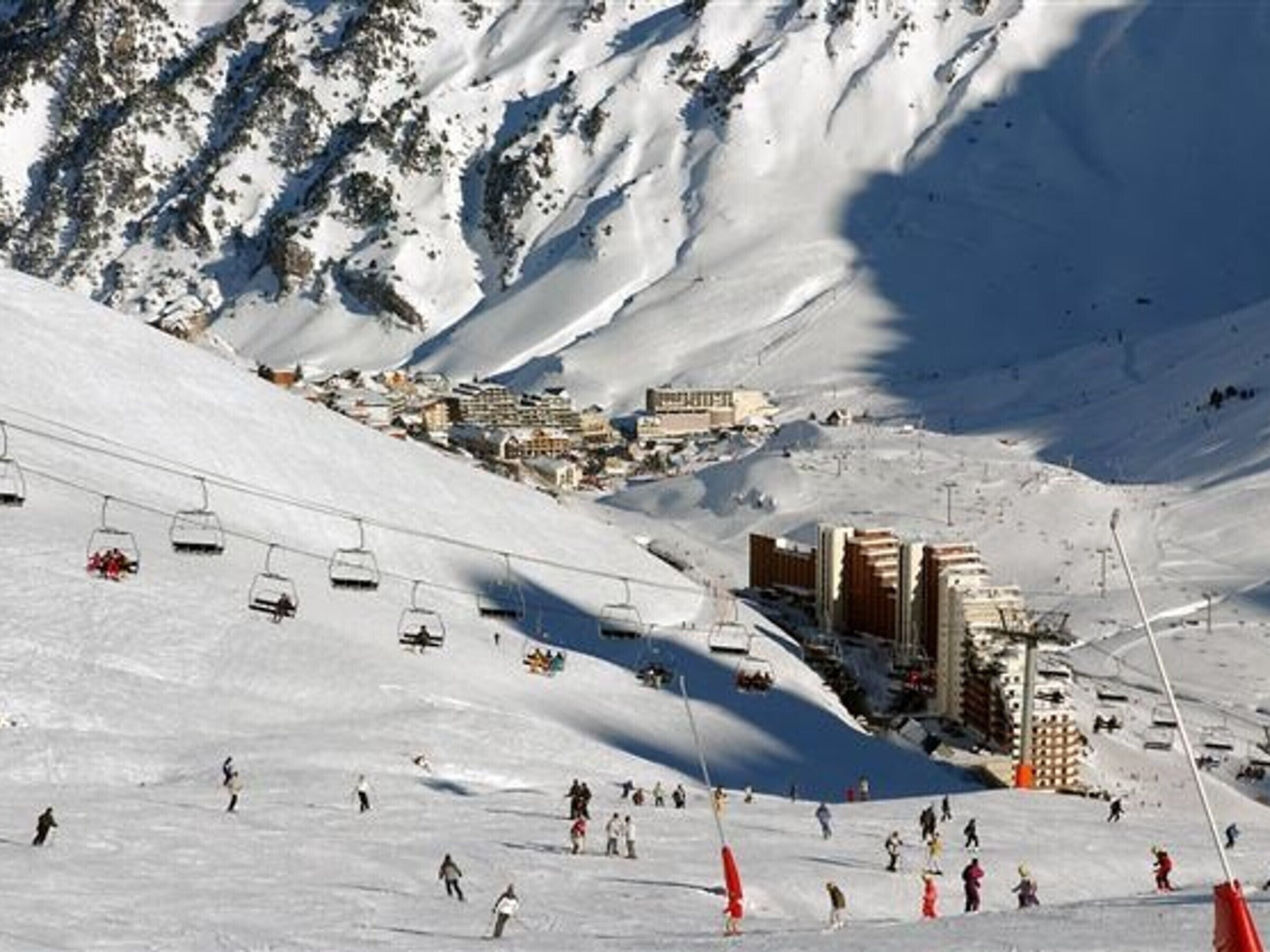 Ein Skigebiet mit Sessellift, Skifahrern und Gebäuden im Hintergrund.