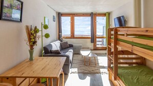 A cozy room with a wooden bunk bed, a sofa, a small table, and a window with curtains. - Studio 4 ppl, south balcony, dishwasher, pets allowed (La Mongie)