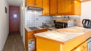 A compact kitchen with wooden cabinets, a microwave, a sink, and a small countertop. - Studio 4 ppl, south balcony, dishwasher, pets allowed (La Mongie)