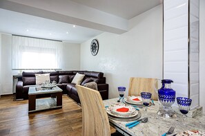 Un salon moderne avec un canapé en cuir marron, une table basse en bois et un coin repas comprenant une table en marbre et de la verrerie bleue.