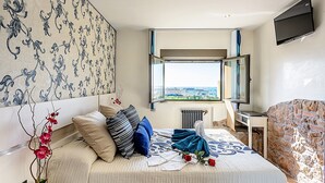 A bedroom with a large bed, a window with a view, a TV mounted on the wall, and a radiator.
