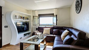 A modern living room with a curved entertainment unit, a leather sofa, and a large window offering a view.