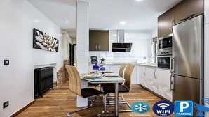 A modern kitchen with stainless steel appliances, a dining area with a wooden table and chairs, and a visible air conditioner.