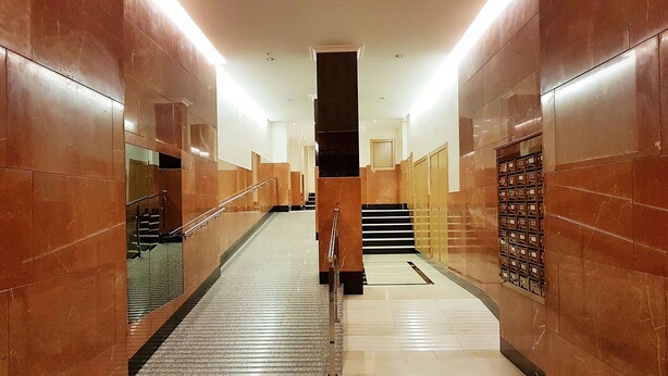 A corridor with marble walls, a handrail, and a staircase leading to a landing.