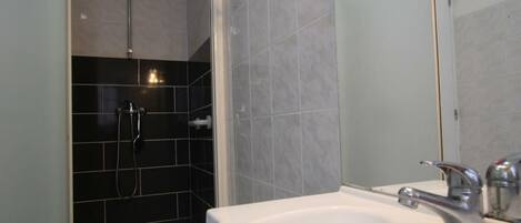 Een badkamer met een wit wastafel, douche en spiegel.