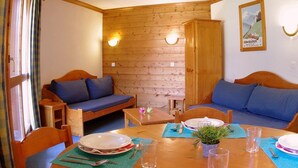 A cozy room with wooden walls, a wooden door, a blue sofa, a wooden table set for two, and a small plant. - Spacious apartment with terrace, 2 bedrooms, pets allowed in Valmorel (Valmorel)