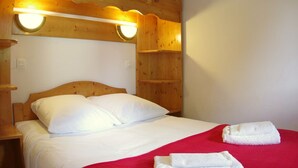 A hotel room with a wooden headboard, two white pillows, a red bedspread, and two rolled towels on the bed. - Spacious apartment with terrace, 2 bedrooms, pets allowed in Valmorel (Valmorel)