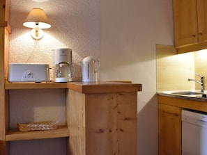 A compact kitchen with a coffee maker, a kettle, and a toaster on a wooden countertop.