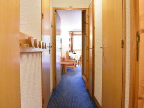 A narrow hallway with wooden doors on either side, leading to a room with a table and chairs.