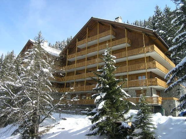 A multi-story wooden building with balconies, surrounded by snow-covered trees.