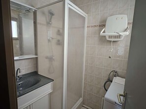 Un bagno con doccia, lavandino e asciugacapelli fissato alla parete.
