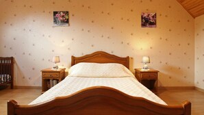 A bedroom with a wooden bed, two bedside tables with lamps, floral wallpaper, and a sloped ceiling. - Charming house in La Hague with fireplace and private yard (La Hague)