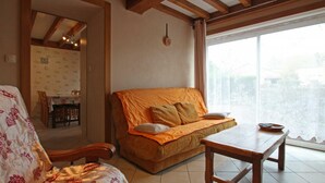 A cozy living room with a sofa, a wooden table, and a patterned armchair. - Charming house in La Hague with fireplace and private yard (La Hague)
