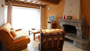 A cozy living room with a fireplace, a sofa, a small table, and a television. - Charming house in La Hague with fireplace and private yard (La Hague)
