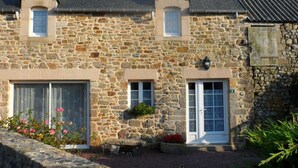 A stone building with a gabled roof, two windows, and a door. - Charming house in La Hague with fireplace and private yard (La Hague)